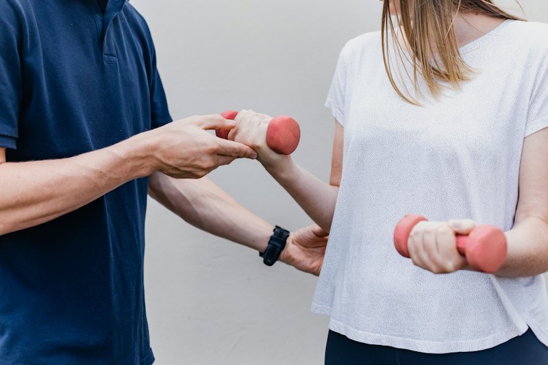 Physiotherapeut führt den Arm einer Patientin bei einer Übung mit Kurzhantel